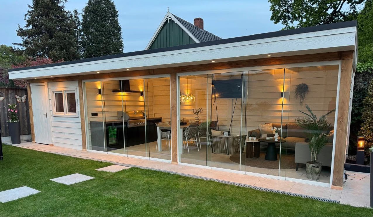 Luxe houten tuinkamer met glazen schuifwanden en verlicht interieur, op maat gemaakt door BijHof in Twente